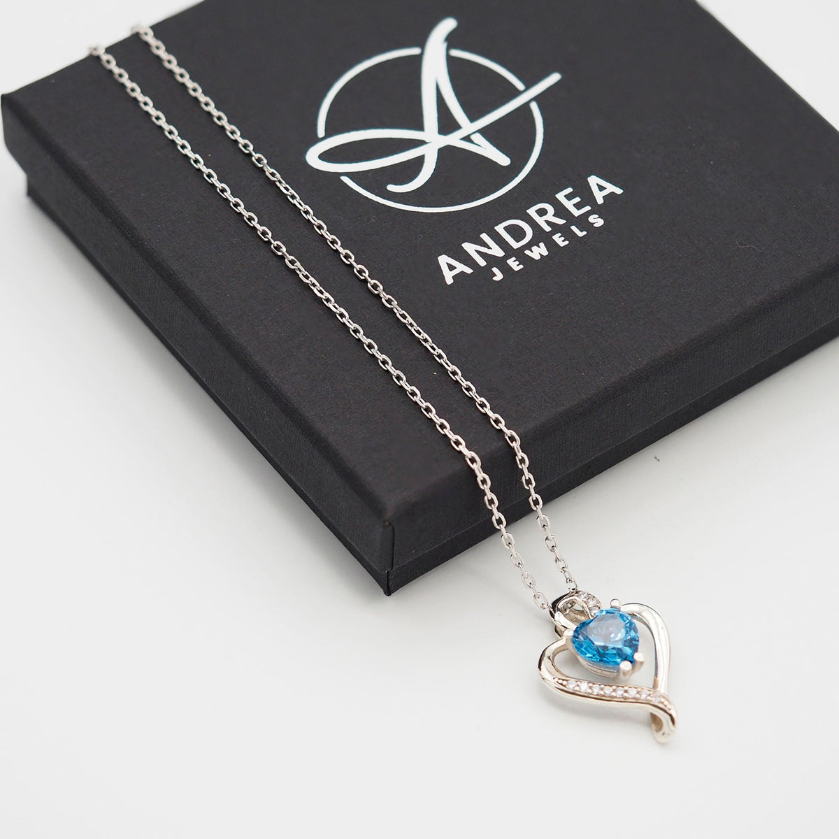 Collar Nina de plata con piedra azul topacio junto a su caja de regalo cerrada - Andrea Jewels