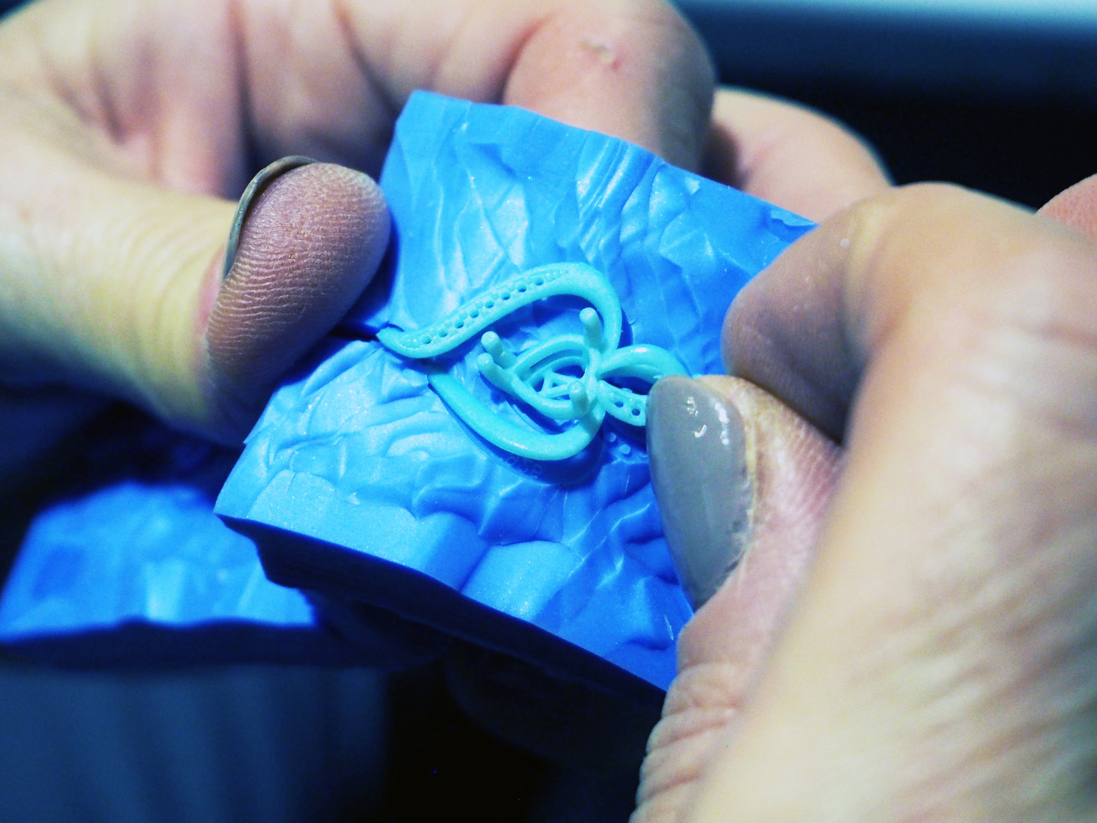 Manos modelando un colgante en cera azul en el taller de Andrea Jewels